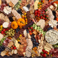A large, beautifully arranged charcuterie board filled with sliced cheeses, crackers, cured meats, fruits, vegetables, pretzels, nuts, and a bowl of dip, photographed from above on a dark surface.